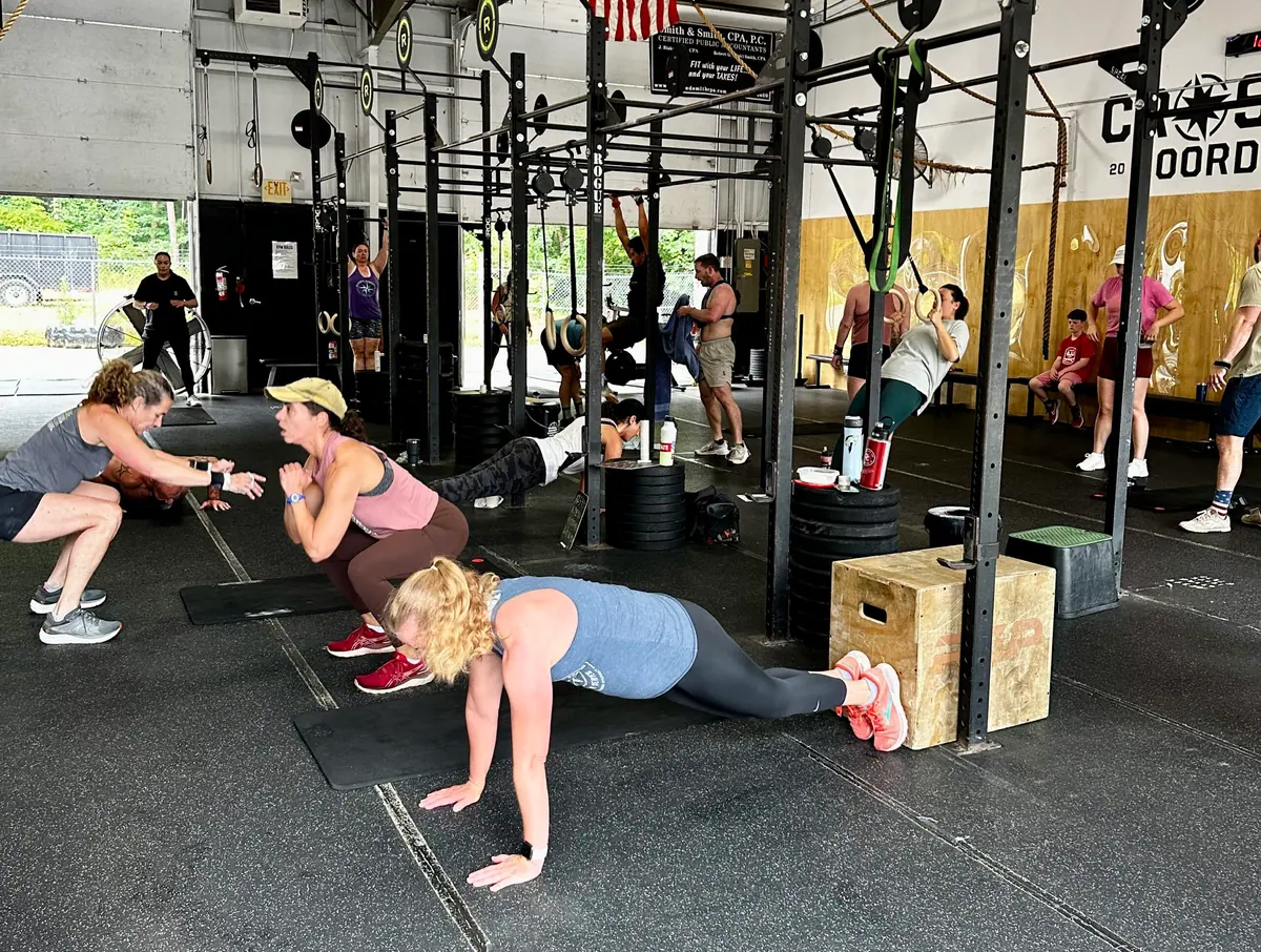Wide view of the CrossFit Coordinate gym floor during Murph — members rotating through push-ups and squats, with scaled push-ups on elevated boxes visible in the background