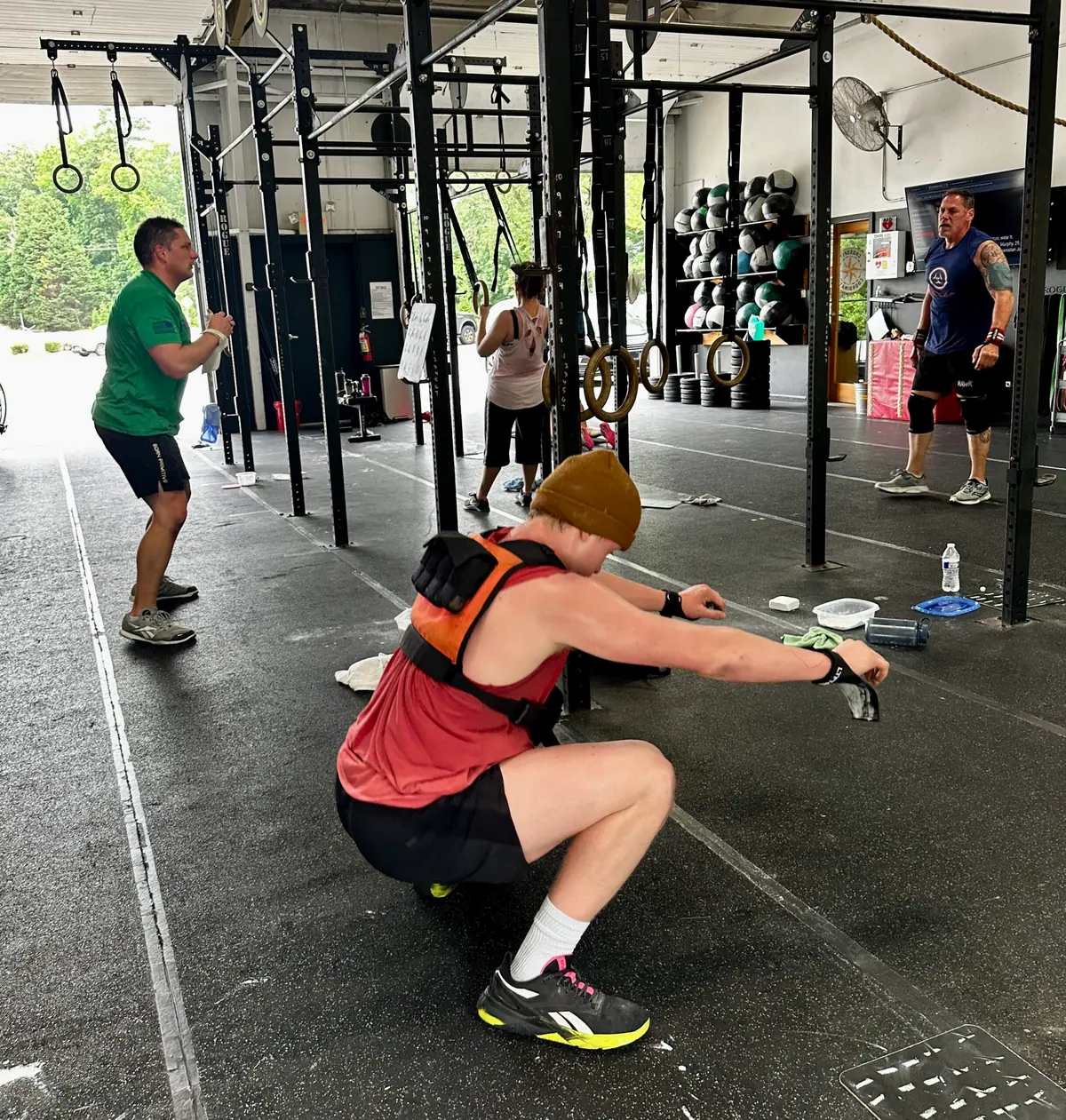 CrossFit Coordinate member doing an air squat in a 20-pound weight vest during Murph, with other members moving through the workout in the background
