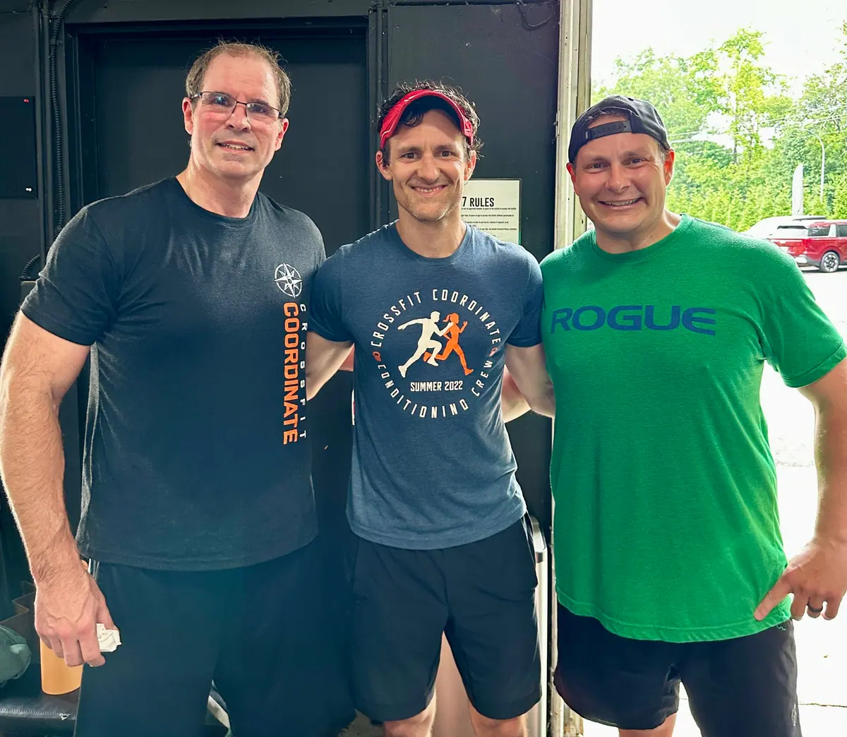 Three CrossFit Coordinate members standing together and smiling after completing Murph — one wearing a CrossFit Coordinate Conditioning Crew shirt