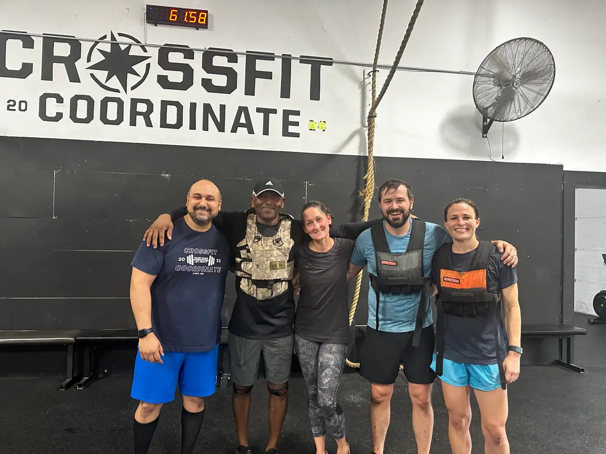 Five CrossFit Coordinate members posing together in weight vests under the CrossFit Coordinate logo after finishing Murph, with the gym clock reading 61 minutes 58 seconds