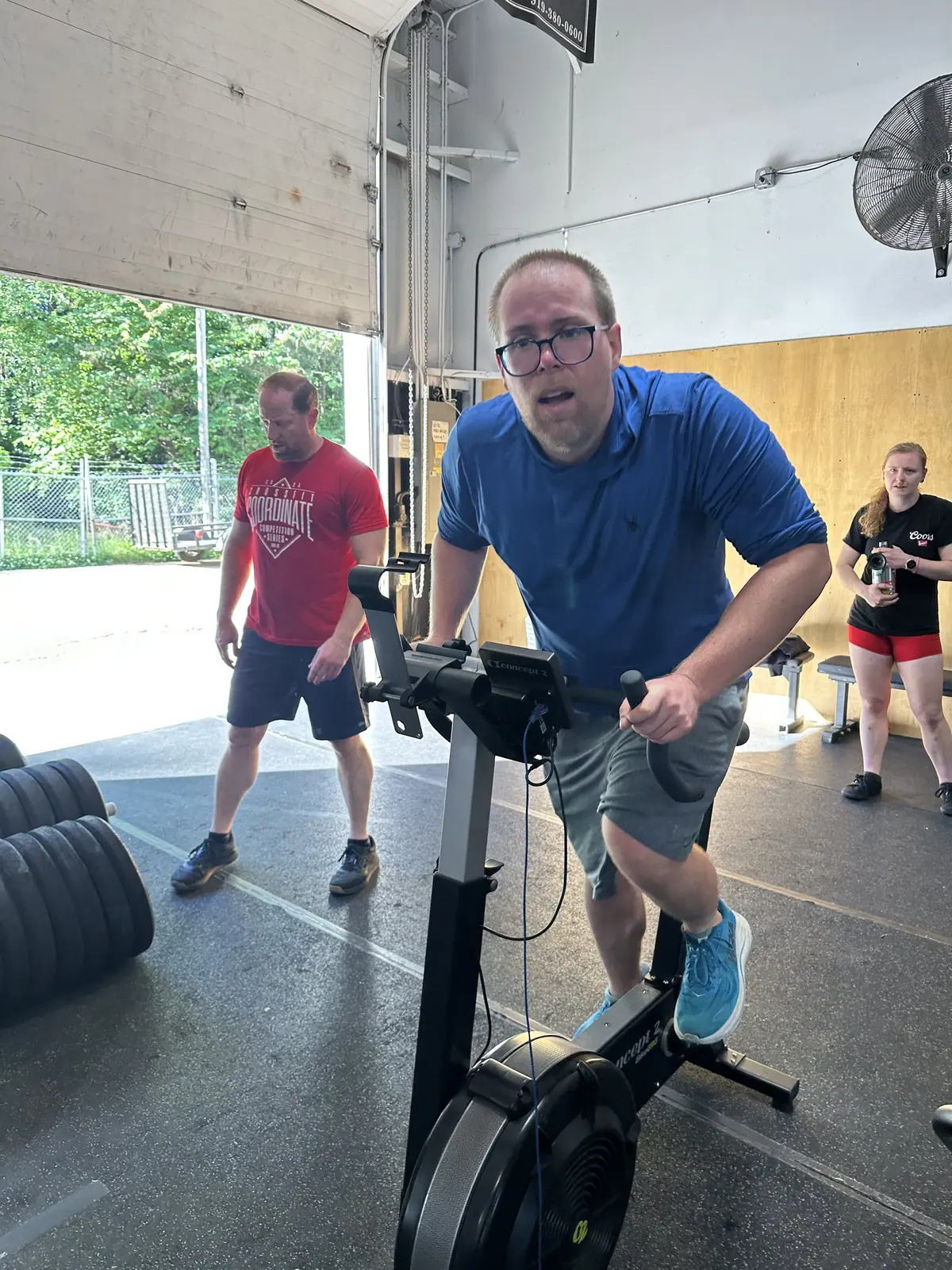 Athlete grinding through the bike erg leg with teammates watching nearby