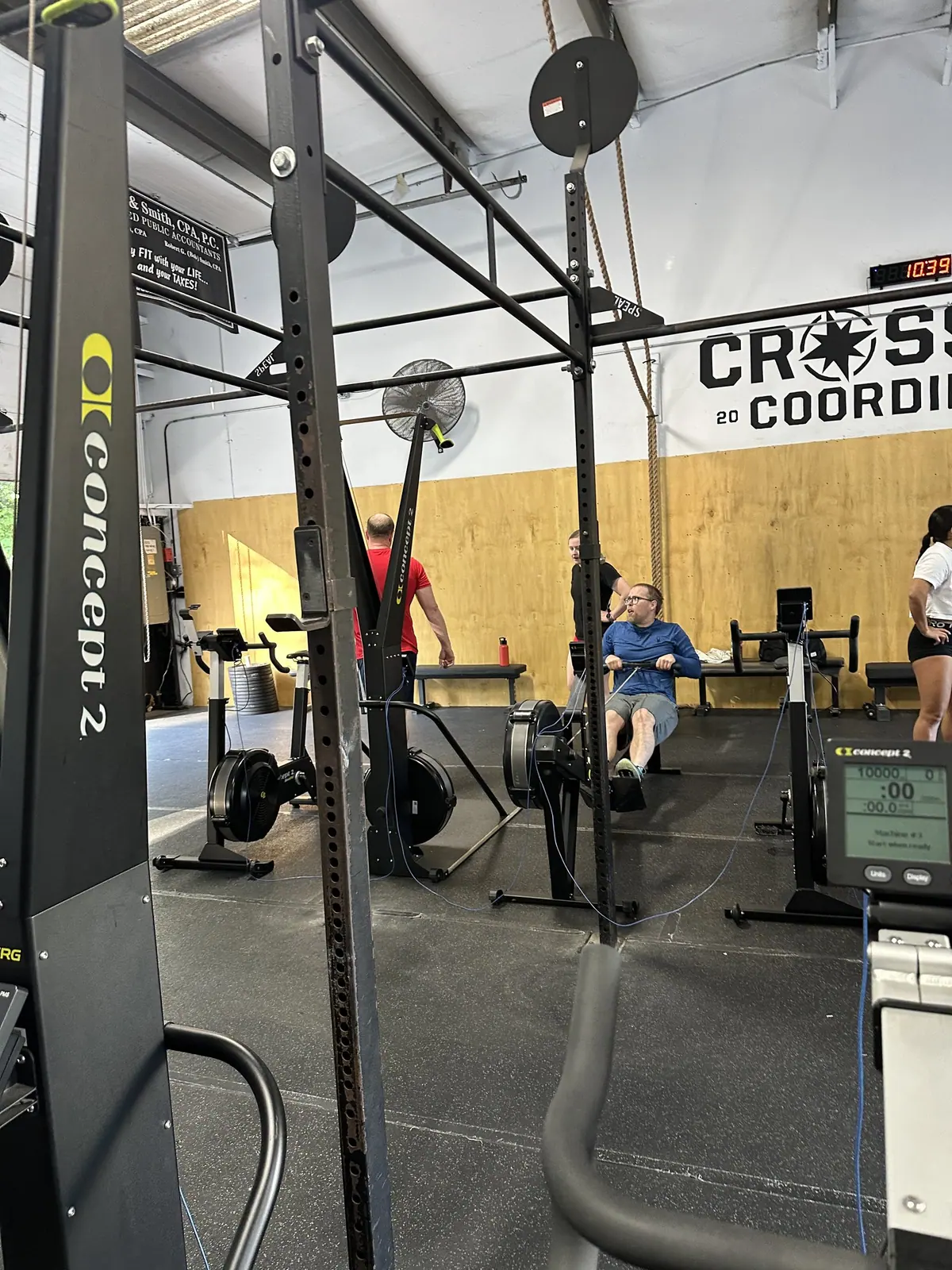 Wide view of the CrossFit Coordinate gym floor mid-Ergathlon, with multiple ergs running at once