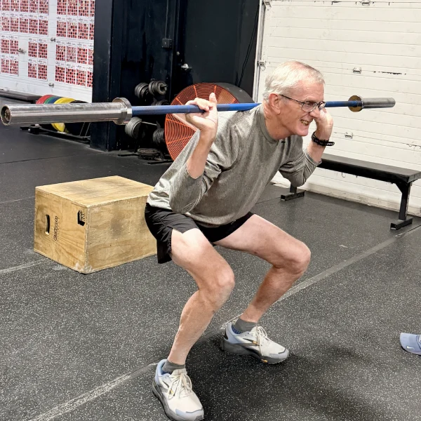 Heinz doing a barbell squat next to a plyo box.